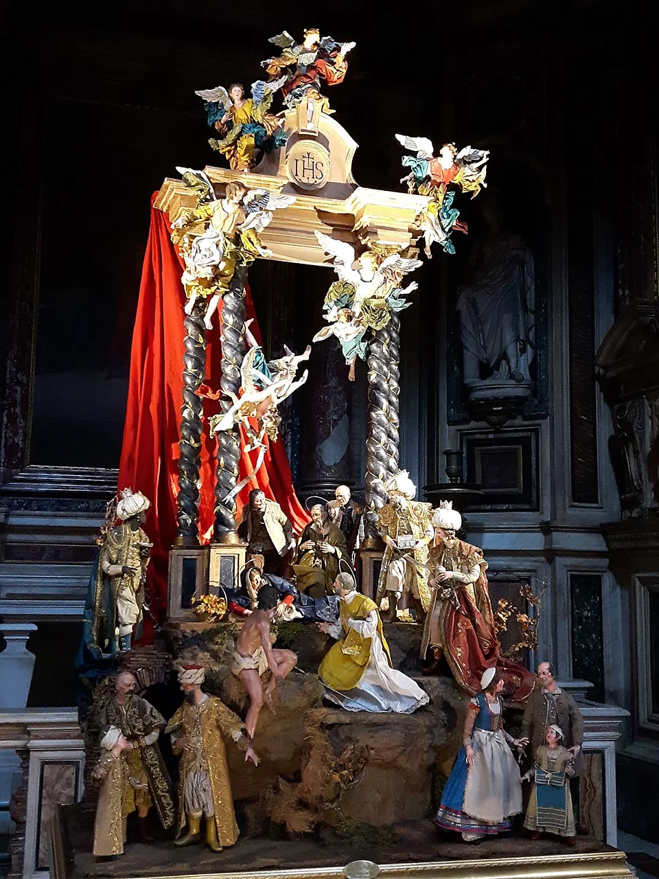 Presepe monumentale allestito su un altare, con drappo rosso e figure artigianali